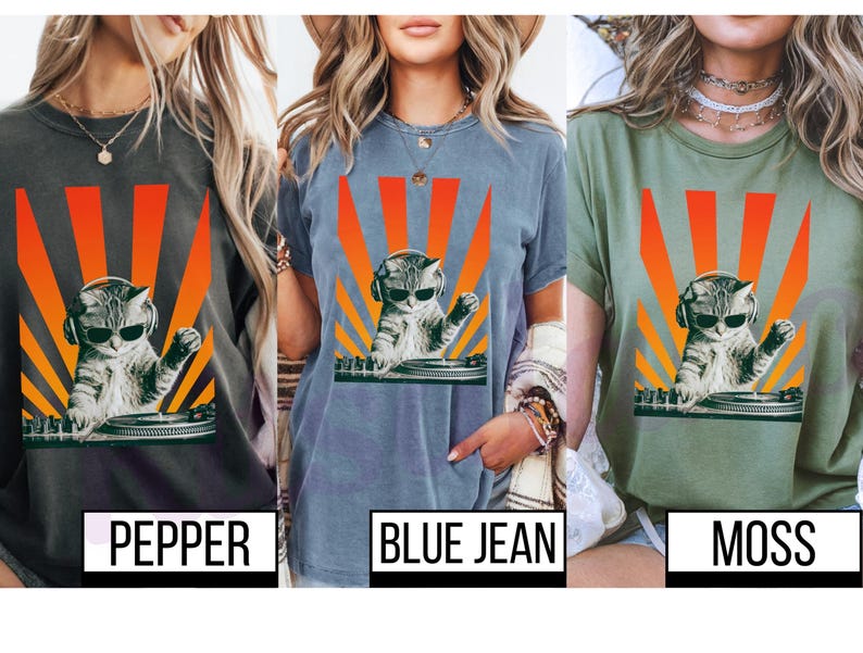 May include: T-shirts in pepper, blue jean, and moss green feature a graphic of a cat DJ wearing sunglasses and headphones, with a retro orange and yellow sunburst design. The shirts have the color names printed below.