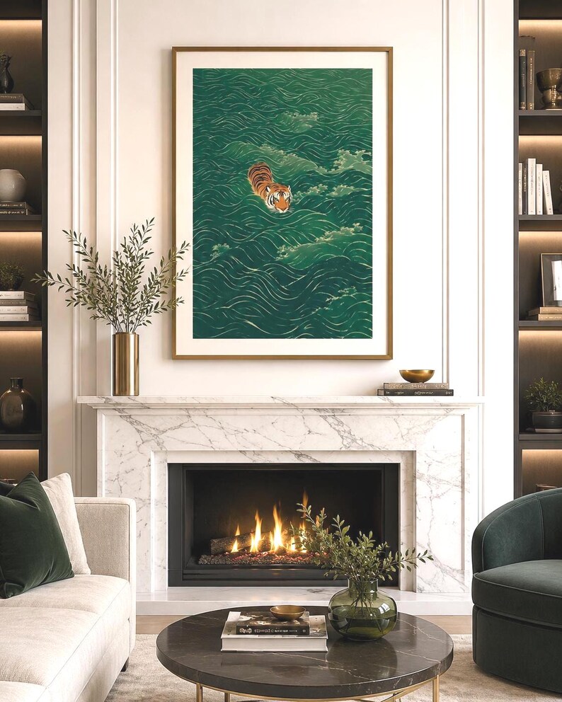 Op de afbeelding: Een ingelijste verticale wandkunstprint met een oranje en zwarte tijger die zwemt in diepgroen water met gestileerde witte golfpatronen. Het kunstwerk is ingelijst in een gouden lijst boven een open haard van wit marmer met een brandend vuur.