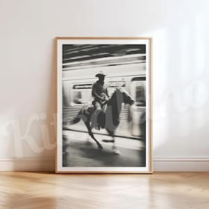 May include: Black and white framed print of a cowboy riding a horse in front of a train. The image is a study in contrasts, with the cowboy and horse in sharp focus against the blurred background of the train. The print is in a wooden frame.