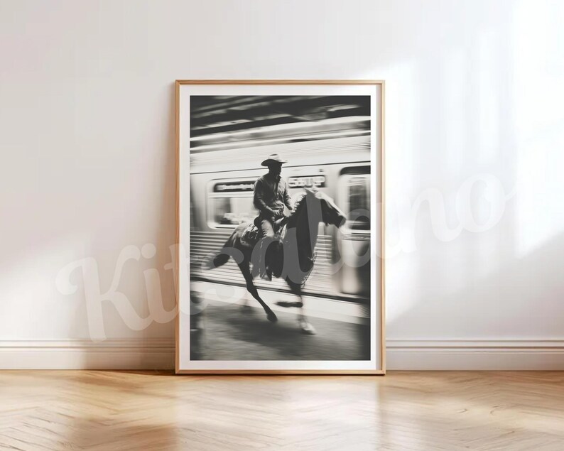 May include: Black and white framed print of a cowboy riding a horse in front of a train. The image is a study in contrasts, with the cowboy and horse in sharp focus against the blurred background of the train. The print is in a wooden frame.