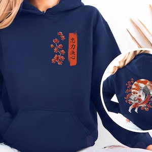 Pode incluir: Um moletom com capuz azul-marinho apresentando um gr&aacute;fico frontal de flores de cerejeira vermelhas e um tra&ccedil;o de pincel laranja vertical com texto japon&ecirc;s. O design traseiro mostra um grande peixe koi nadando diante de um sol vermelho.