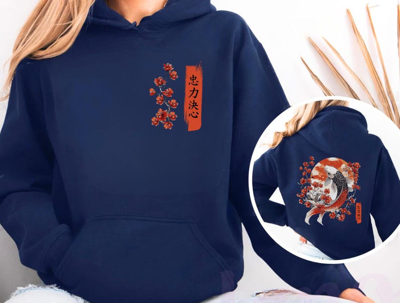 Pode incluir: Um moletom com capuz azul-marinho apresentando um gr&aacute;fico frontal de flores de cerejeira vermelhas e um tra&ccedil;o de pincel laranja vertical com texto japon&ecirc;s. O design traseiro mostra um grande peixe koi nadando diante de um sol vermelho.