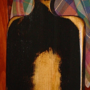 May include: A wooden cutting board with a black and brown finish. The board has a handle and is slightly curved.