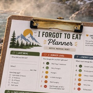 May include: A cork clipboard holding an I Forgot To Eat Planner with sections for last meal, hunger level, energy level, food options, protein, water, and reminders. The planner features mountain graphics and a yellow pencil rests beside it.
