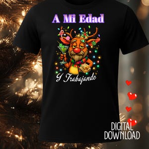 Peut inclure: T-shirt noir avec un renne de dessin animé tenant un martini et un cadeau. Le texte "A Mi Edad Y Trabajando" est au-dessus et en dessous du renne. Le renne a un nez rouge, une écharpe colorée et est décoré de lumières de Noël.