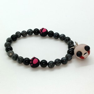 May include: A beaded bracelet featuring dark gray and black beads. The bracelet includes two black paw print charms with pink details and a panda bear charm with black and red accents. Jewelry.