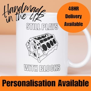 May include: White ceramic mug featuring a black and white engine block graphic. The mug has the text "STILL PLAYS WITH BLOCKS". Additional text includes "Handmade in the UK" and "Personalisation Available". An orange circle states "48HR Delivery Available".