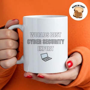 Op de afbeelding: Een witte keramische mok met een zwart handvat. De mok heeft de tekst "Worlds Best Cyber Security Expert" erop gedrukt in het zwart. Een klein zwart-wit laptop-icoon bevindt zich onder de tekst.