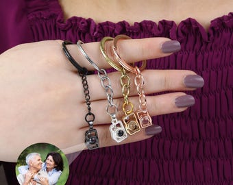 May include: Four silver, gold, rose gold, and black keychains with a camera charm. Each camera charm has a small clear window that reveals a photo inside.