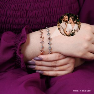 Könnte beinhalten: Zwei zarte Armbänder, eines in Roségold und eines in Silber, jeweils mit floralen und Edelstein-Akzenten. Die Armbänder werden an einem Handgelenk vor tiefviolettem Stoff gezeigt. Ein kleines rundes Bild zeigt ein Paar.