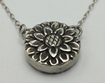May include: A silver necklace with a round pendant featuring a detailed floral design.