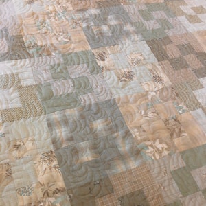 K&ouml;nnte beinhalten: Eine Decke aus verschiedenen Braunt&ouml;nen und Gr&uuml;nt&ouml;nen mit einem gesteppten Muster aus geschwungenen Linien. Die Decke besteht aus Patchwork-Quadraten in verschiedenen Gr&ouml;&szlig;en und Mustern.