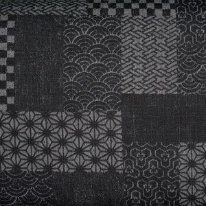 Puede incluir: Tela negra y blanca con un diseño de patchwork que presenta varios patrones geométricos. La tela tiene una superficie texturizada y un brillo sutil.