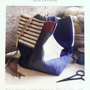 Könnte beinhalten: Eine blaue, weiße und rote Patchwork-Stofftasche mit Kordelzug und einem weißen und schwarzen gestreiften Stoffpanel. Die Tasche liegt auf einer Holzoberfläche mit einer Schere und einer Spule Garn.
