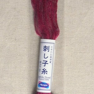 Puede incluir: Una bobina de hilo de bordar rojo con la etiqueta "Sashiko Thread Cotton 100% Olympus" en japonés e inglés. La etiqueta también incluye el texto "刺し子糸" que se traduce como "Sashiko Thread" en inglés.