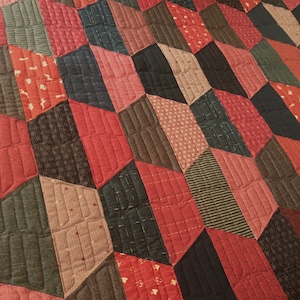 May include: A quilt made of various fabrics in shades of red, brown, and black. The quilt is made up of squares and rectangles, and the fabric has a variety of textures and patterns.