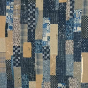 Op de afbeelding: Textielkunstwerk met een patchworkontwerp in blauw, beige en wit. Het ontwerp bevat verschillende patronen, waaronder geometrische vormen en cirkelvormige stiksels. De esthetiek doet denken aan traditionele Japanse textiel.