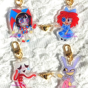 May include: Four acrylic keychains with cartoon characters, each attached to a gold-colored clasp. The characters include a jester, a doll, a crying figure, and a purple rabbit. Each keychain has the text "KOTYA GRAVEYARD".