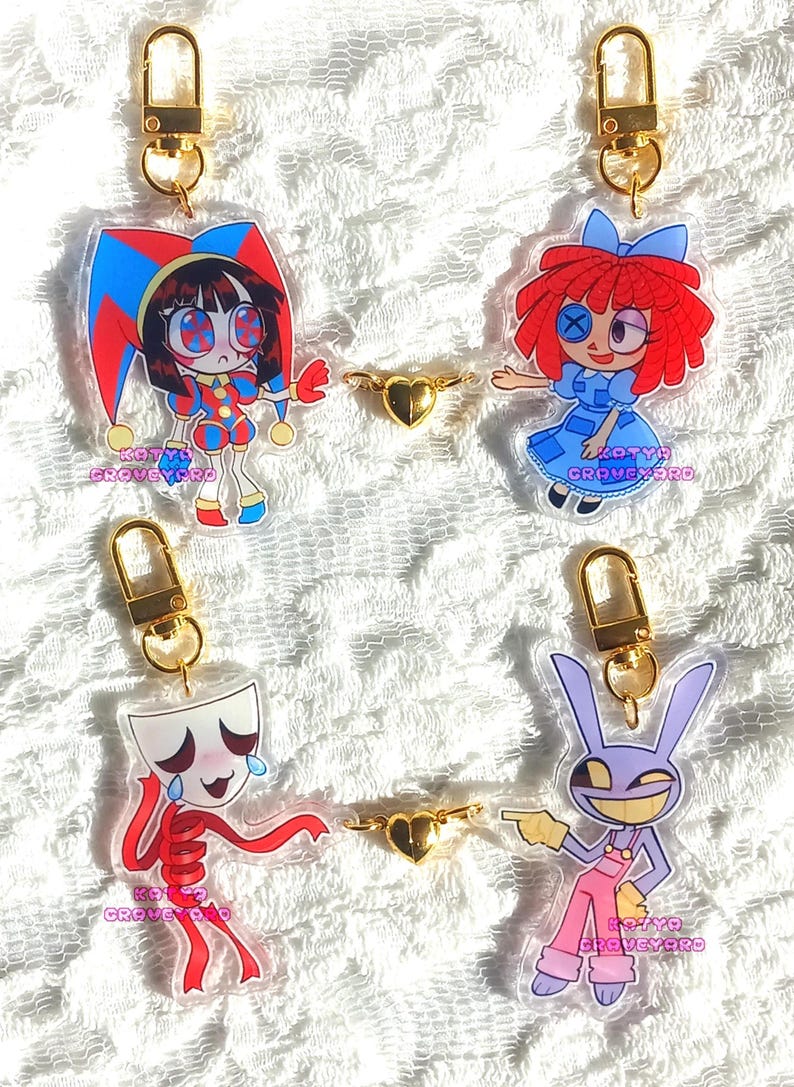 May include: Four acrylic keychains with cartoon characters, each attached to a gold-colored clasp. The characters include a jester, a doll, a crying figure, and a purple rabbit. Each keychain has the text "KOTYA GRAVEYARD".