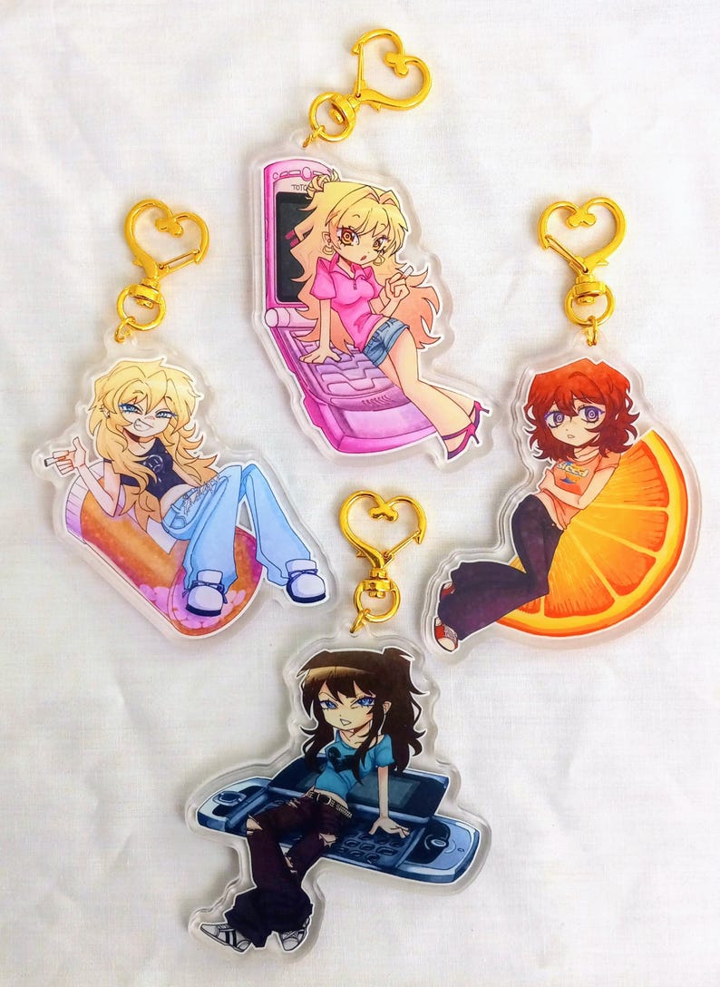 May include: Five acrylic keyrings with anime-style illustrations of characters in different poses. Each keyring has a gold-coloured heart-shaped clasp. The characters are depicted on a pill, a phone, a slice of orange, and a game console.