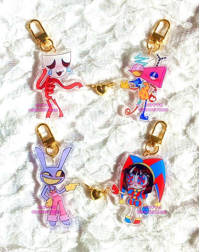 May include: Four acrylic keychains with gold-colored hardware. Each keychain features a unique cartoon character design. The characters include a crying skeleton, a robot-like figure, a purple rabbit, and a jester. The text "KATYA GROVEYARD" is printed on each keychain.