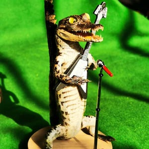 May include: A taxidermied alligator holding a black electric guitar and standing on a wooden base with a microphone stand.