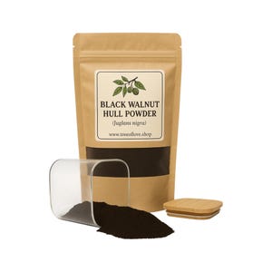 May include: A brown paper bag labeled "BLACK WALNUT HULL POWDER" with a clear container and a wooden lid. The container holds a pile of dark brown powder. The bag has a white label with a green illustration of walnuts.