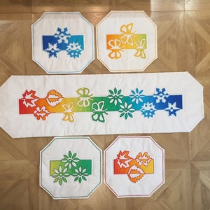 May include: Set of five white fabric placemats with colourful embroidered designs. The designs include butterflies, snowflakes, leaves, and flowers. The placemats are rectangular and octagonal in shape.