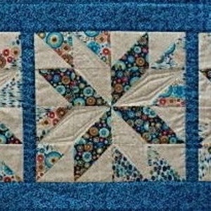 May include: A blue and white quilt with a starburst pattern. The quilt is made up of multiple squares with a white background and blue and white floral print.