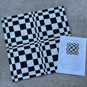 May include: A black and white checkered fabric square with a disappearing four-patch design. A printed paper with instructions and a diagram is next to the fabric. The paper is titled "Disappearing 4 Patch".