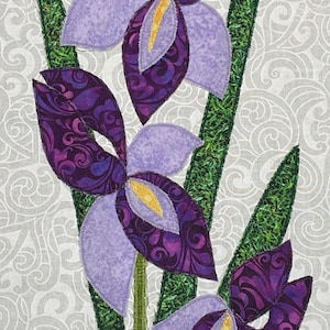 Puede incluir: Una obra de arte textil con tres flores de iris estilizadas. Las flores tienen pétalos morados con centros estampados y detalles amarillos. Los tallos y hojas verdes son visibles sobre un fondo gris claro con un patrón de remolinos.