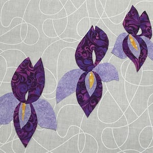 May include: Three stylized iris flowers in shades of purple and lavender are arranged on a gray background with white swirling lines. The flower petals have a patterned design, and the centers are yellow.