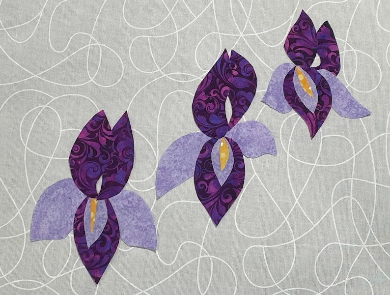 May include: Three stylized iris flowers in shades of purple and lavender are arranged on a gray background with white swirling lines. The flower petals have a patterned design, and the centers are yellow.