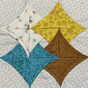 May include: A quilt block with four diamond-shaped fabric pieces. The top diamond is white with a small blue and white pattern, the right diamond is yellow with a brown polka dot pattern, the bottom diamond is brown with a small white square pattern, and the left diamond is blue with a white leaf pattern.