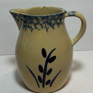 Puede incluir: Jarra de cerámica beige con asa curva y boquilla. El borde y el asa están decorados con un patrón moteado azul. Un diseño floral azul está pintado en la parte delantera. Diseño clásico y rústico.