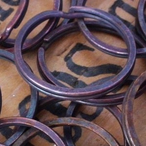 May include: A close-up of a pile of copper key rings. The rings are stacked on top of each other and have a shiny, metallic finish.