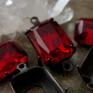 May include: Four red glass cabochons with black metal settings. The cabochons are faceted and have a shiny finish.