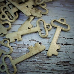 May include: A collection of antique-style keys in a warm, aged brass color. The keys are scattered on a weathered, white-painted wooden surface, creating a vintage aesthetic. The keys have intricate designs and are ideal for crafting or decorative purposes.