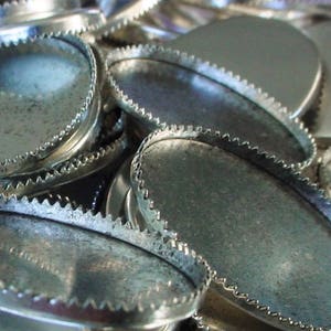 May include: A pile of silver metal oval-shaped blanks with scalloped edges.