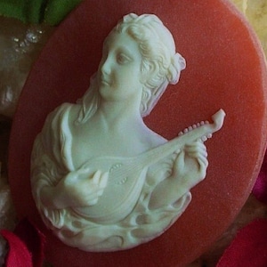 May include: A white cameo of a woman playing a lute, set against a red background.