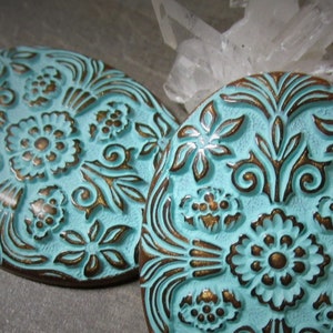 May include: Two turquoise blue and gold oval-shaped decorative tiles with an embossed floral design.