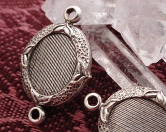 May include: Two silver-toned metal pendant charms with a decorative oval frame and a textured surface. Each charm has two loops for attaching to a necklace or bracelet.