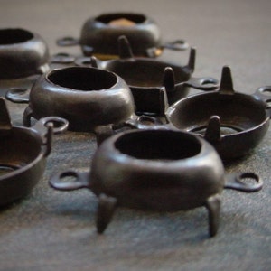 May include: Close-up of a group of black metal settings for cabochon stones. The settings have four prongs and a round base.
