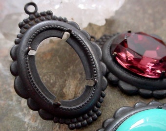 May include: A set of three silver-toned metal pendant settings with scalloped edges. The settings are oval shaped and have a raised border. One setting is empty, while the other two have a pink and a turquoise cabochon stone.