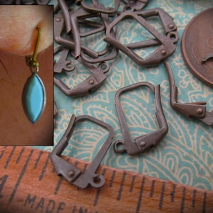 May include: A close-up of a group of 10 silver-toned earring hooks. The hooks are made of metal and have a simple, elegant design. The hooks are arranged in a random pattern on a blue and white patterned fabric.