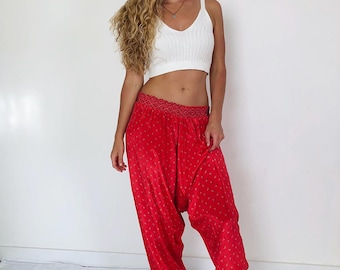May include: Red harem pants with a small gold pattern and a decorative waistband. The pants are paired with a white ribbed crop top and gold sandals. The outfit is casual and comfortable.