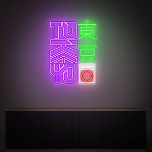 May include: Neon sign with the word "TOKYO" in purple and green. The Japanese characters are illuminated with neon lights. The sign also includes a white box with a red circle and the word "JAPAN".