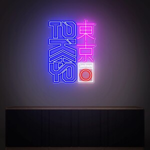 May include: Neon sign with the word "TOKYO" in blue and Japanese characters in pink. The sign includes a white rectangle with a red circle and the word "JAPAN". The sign is mounted on a dark wall.