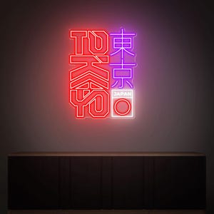 May include: Neon sign displaying the word "TOKYO" in red and Japanese characters in purple. The word "JAPAN" is below the Japanese characters, with a white circle. The sign is mounted on a dark wall above a wooden cabinet.
