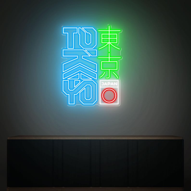 May include: Neon sign with the word "TOKYO" in blue and green, with Japanese characters. The sign includes a red and white circle with the word "JAPAN" below it. The sign is mounted on a dark wall above a dark cabinet.